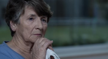 Elderly person holding a photo and sitting with a supportive companion on a garden bench, symbolizing comfort and healing after losing a loved one.