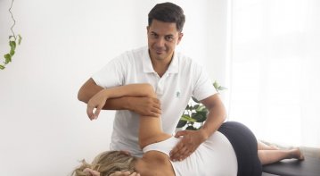 A physiotherapist guiding a patient through targeted shoulder exercises using resistance bands and manual therapy, aimed at relieving shoulder pain and improving mobility.