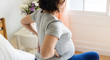 Pregnant woman practicing gentle yoga at home as part of lifestyle changes to support chronic pain management during pregnancy