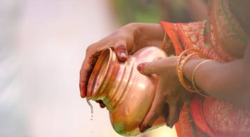 A traditional Chhath Puja celebration showing devotees standing in a river at sunrise, offering prayers and fruits to the Sun God with decorated bamboo baskets.